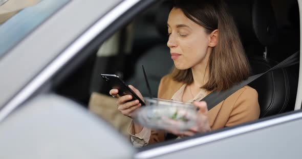 Woman Typing on a Smart Phone While Having a Snack in a Vehicle alt