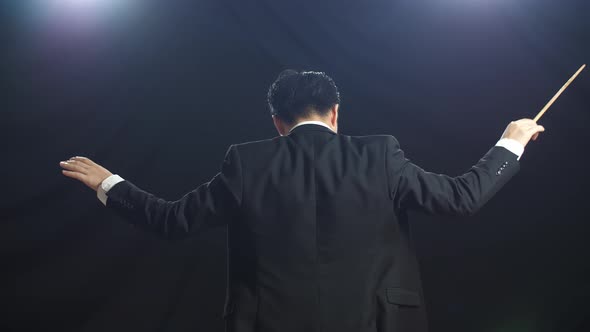 Back View Of Asian Conductor Man Holding A Baton And Showing Gesture In The Black Studio alt