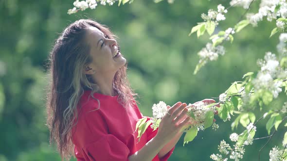Happy Woman in Blooming Garden in Springtime Laughing and Playing with Branch of Tree with Blossoms alt