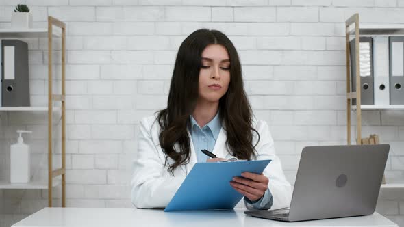 Female Doctor Taking Notes And Nodding Head Sitting In Office alt