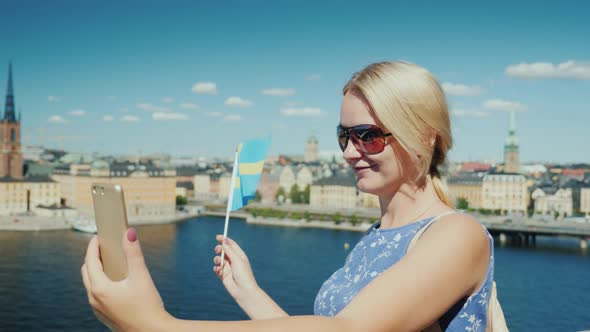 A Happy Tourist with the Flag of Sweden Takes Pictures of Himself Against the Backdrop of Stockholm alt