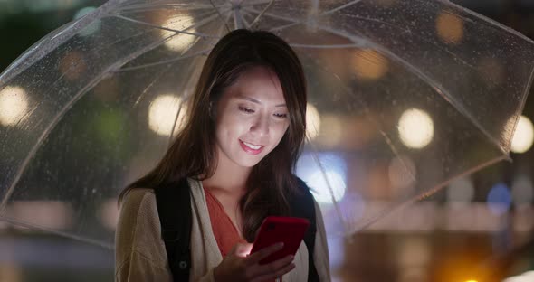 Woman hold with umbrella and use of mobile phone in the city at night alt