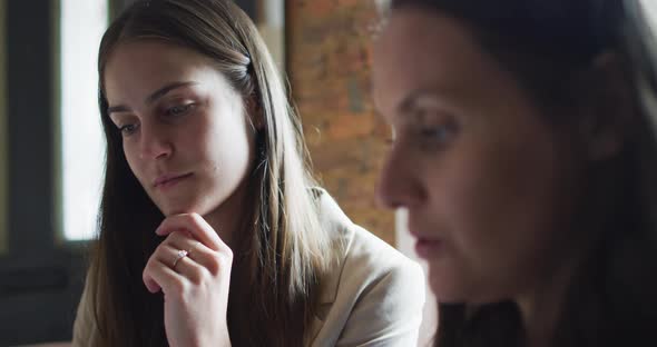 Portrait of two caucasian businesswomen sitting at table, talking, having business meeting alt