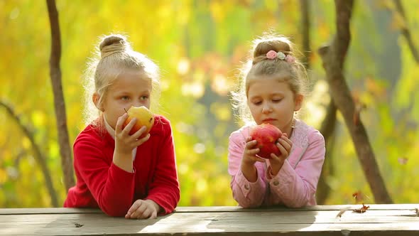 Two little girls eating a natural apples ,outdoors . Two little girls eating a natural apples
