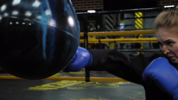 A Beautiful Young Woman in Blue Boxing Gloves Hits a Punching Bag in the Gym alt