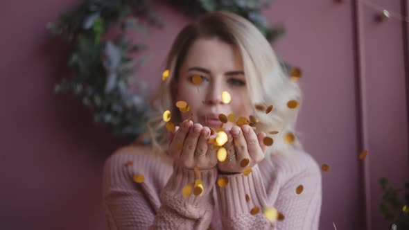 Beautiful Woman in Sweater Blows Shiny Confetti From Her Hands To the Camera in Slow Motion alt