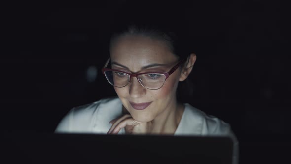 Reflection of the Screen with Glasses. Portrait of a Business Woman Working Late on a Laptop. alt
