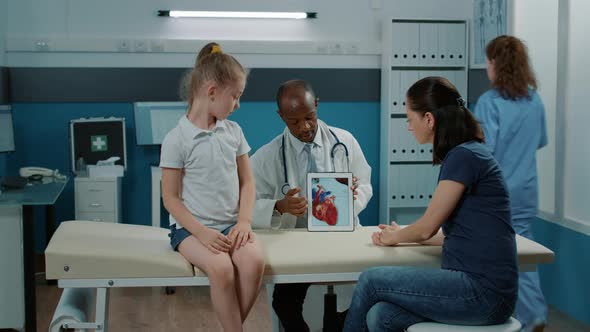 Medic Showing Cardiology Diagnosis on Tablet to Mother and Kid alt