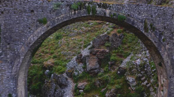 Backward moving aerial of couple standing on top of natural inter mountainous bridge during hiking. alt