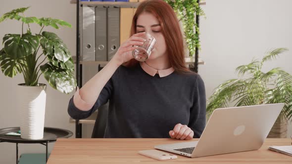Red hair female student drinking water at work. Refreshment for businesswoman