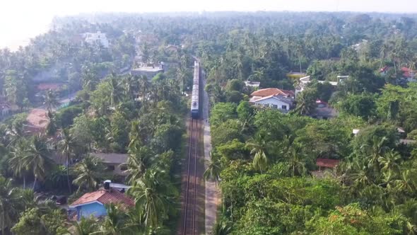 Slow Motion Aerial Shot the Old Train Rides Through the Tropics with Palm Trees and Villas alt