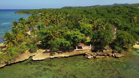 Tropical travel destination with green lush palm trees on rocky coastline with clear shallow water, alt