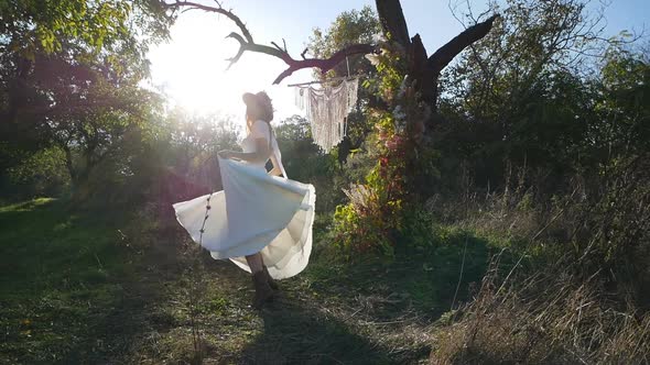 A young beautiful brunette in a white dress rotates and waves her dress on a meadow in the forest. S alt