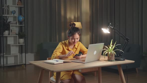 Asia Woman With Laptop Computer Calling On Smartphone From Home At Night alt