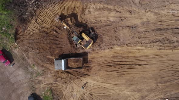 Aerial top view: yellow excavator pouring soil into tipper. alt