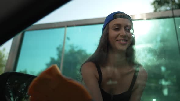 Front View Young Woman Rubbing Side Window Glass of Car in Slow Motion Smiling alt