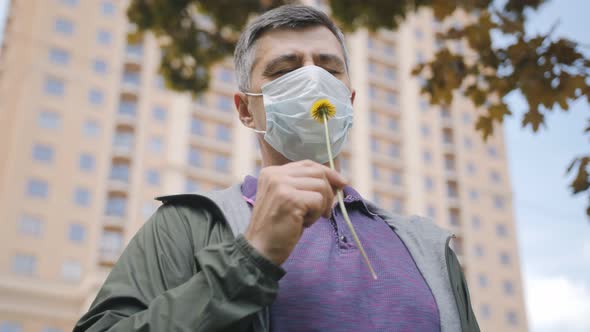 A Man Wearing a Medical Mask on His Face Sniffs a Flower in the City Center