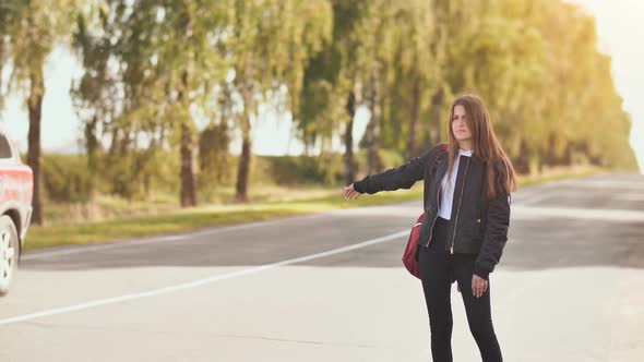 A Young Girl of 17 Years Old Stands on the Road and Tries to Stop Any Car alt