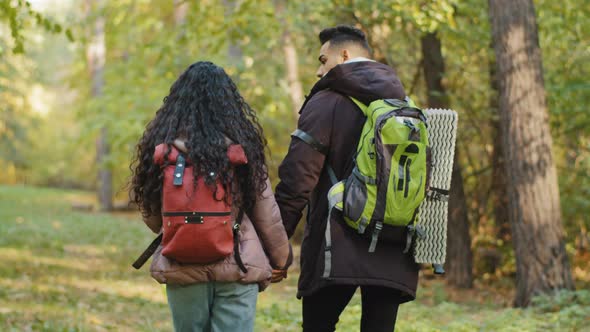 Back View Young Active Healthy Couple in Love Tourists Travelers Travel with Backpack in Forest Walk alt