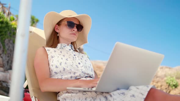 Beautiful Woman Works Using Laptop on Sea Beach Sunbed in Summer
