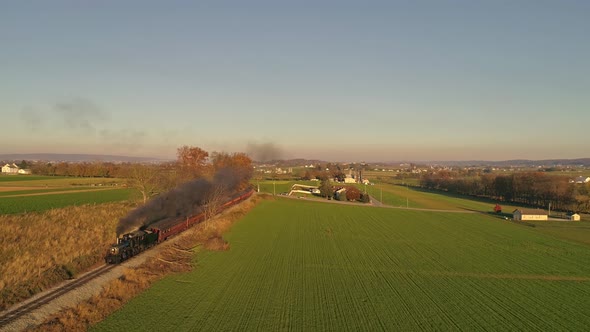 Aerial View of an Antique Steam Locomotive Approaching Pulling Passenger Cars and Blowing Smoke and Steam During the Golden Hour in late Afternoon alt