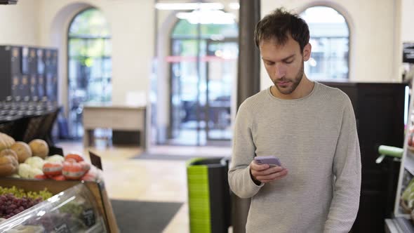 Relaxed Man Walking Through the Store Looking at the Screen of His Smartphone alt