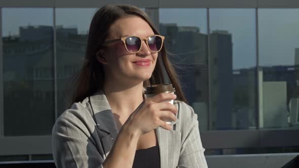 Smiling Young Woman in Sunglasses Drinks Coffee From a Disposable Cup