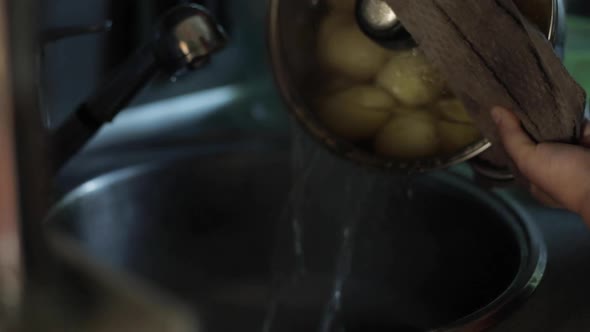 A Housewife Woman Drains Water From a Pot From a Boiled Potato Into the Sink