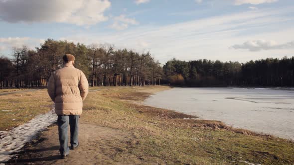 elderly retired man walks in a city park by the lake. winter walk. loneliness.