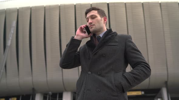 Businessman wearing a coat and talking on the phone alt