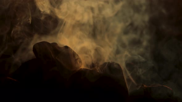 Charcoal smolders getting ready for outdoor cooking. The sun highlights the threads of fumes emanati alt