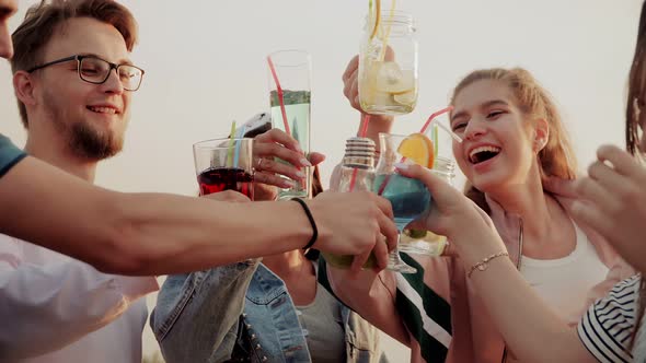 The Friends Enjoy Their Summer Urban Cocktails Standing on the Roof of the House and Clinking alt