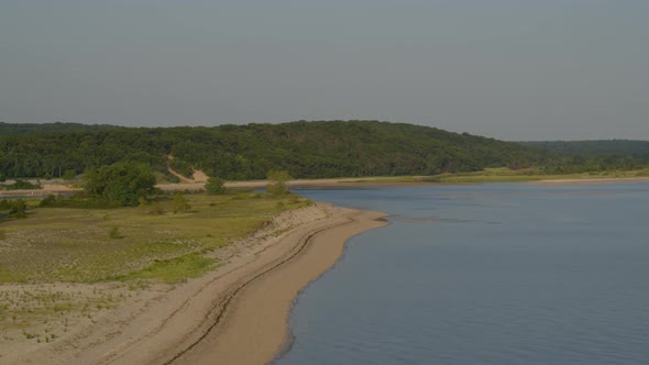 Forward Aerial Pan of a Sandy Beach Shore Near Dense Forest Trees alt
