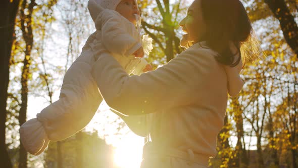 Baby in mom's arms in the park with yellowed leaves