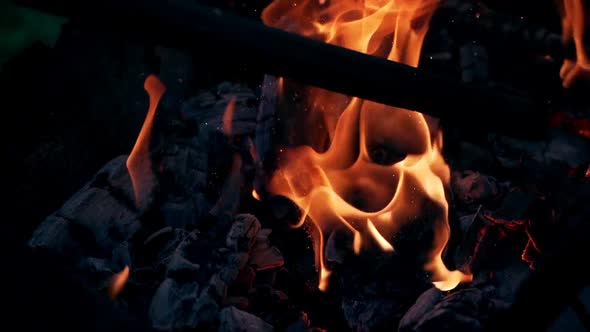 Explosion of flame with bright sparks. Black smoldered logs explode with fiery flame alt