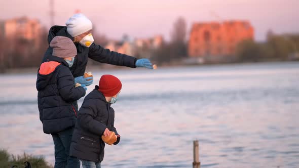 Mother, son and daughter in medical masks feed ducks in the Park on the lake.