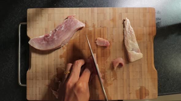Carefully slicingr raw pork meat on a bamboo chopping board with a stainless steel chef knife - Top alt