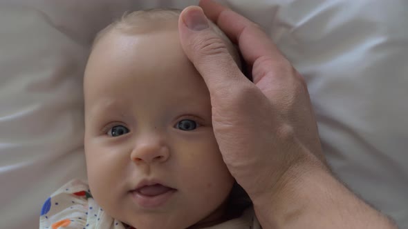 A Closeup of a Baby Girl's Face and a Father's Hand Touching Her alt