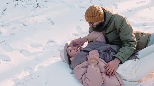 Romantic Happy Couple Lies in the Snow and Laugh on Sunny Day Enjoying Life