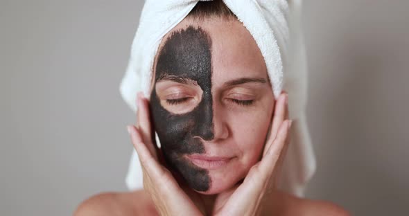 Caucasian woman looking on camera while doing skin care treatment with black facial mask alt