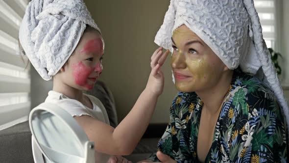 Little Girl with a Cosmetic Mask on Her Face Helps Her Mother To Make a Cosmetic Mask alt