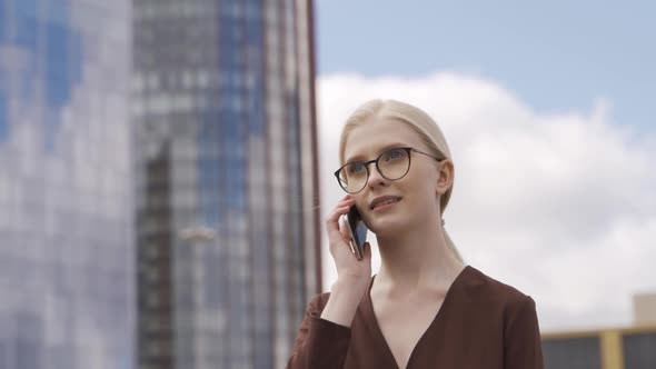 Business Confident Woman Talking on the Phone and Walking Past Modern Skyscrapers