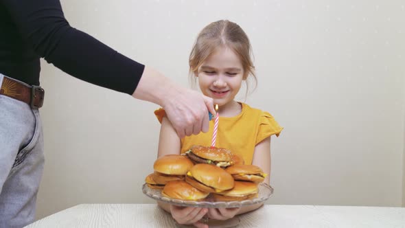 a Funny Little Girl Makes a Wish and Blows Out a Candle on a Hamburger Cake alt