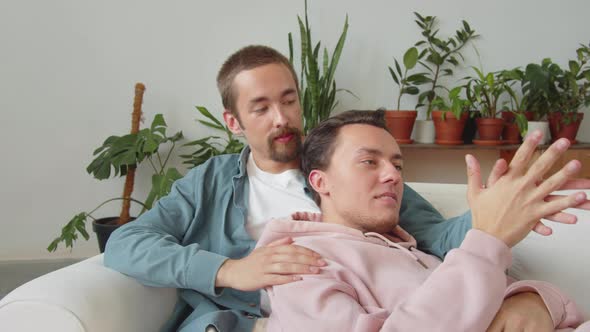 Two Lgbt Men are Sitting Together on the Sofa in the Living Room Talking and Holding Hands alt