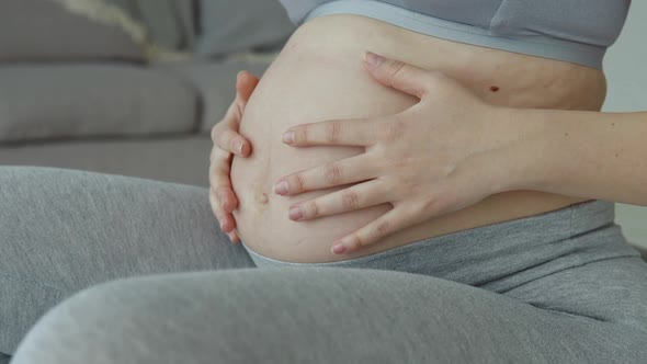 A Pregnant Woman in Sportswear Sits on a Fitball and Holds Her Hands on Her Stomach alt