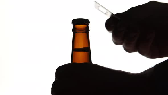 The Silhouette of Male hands opening brown beer bottle with opener