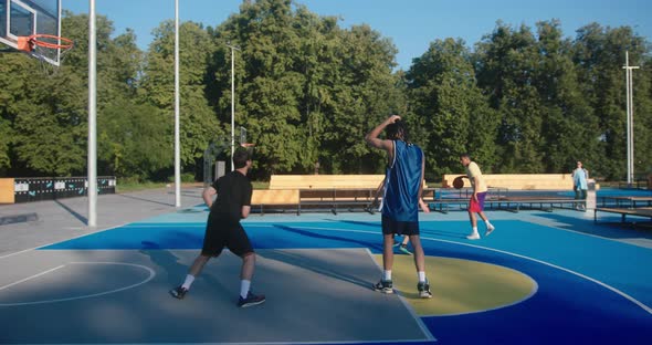 Basketball Players Play Fairgame on Blue Court Against Trees alt