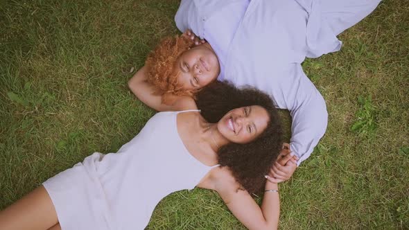 Young Beautiful Happy Lesbian African American Couple Lying on Grass Laughing Stretching Out Hands