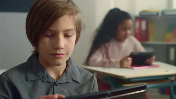 Smiling Schoolboy Sitting at Desk with Digital Tablet in Elementary School alt