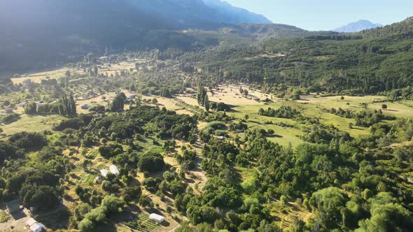 Pan left flying above El Hoyo valley surrounded by a beautiful woodland and mountains in background, alt